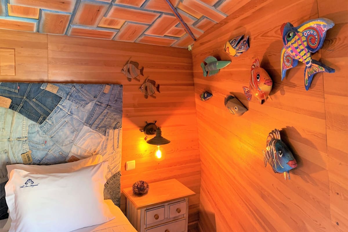 Ein Zimmer mit Holzwänden, einem Bett mit Jeansbezügen, einem Nachttisch und dekorativer Fischwandkunst.