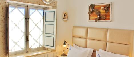 A bedroom with a bed, a nightstand, a lamp, a window with shutters, and a wall decoration.