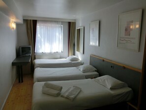Een hotelkamer met twee enkele bedden, een bureau met een televisie en een raam met gordijnen.