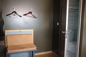 Een kamer met een bankje, twee wandhaakjes en een badkamers deur.