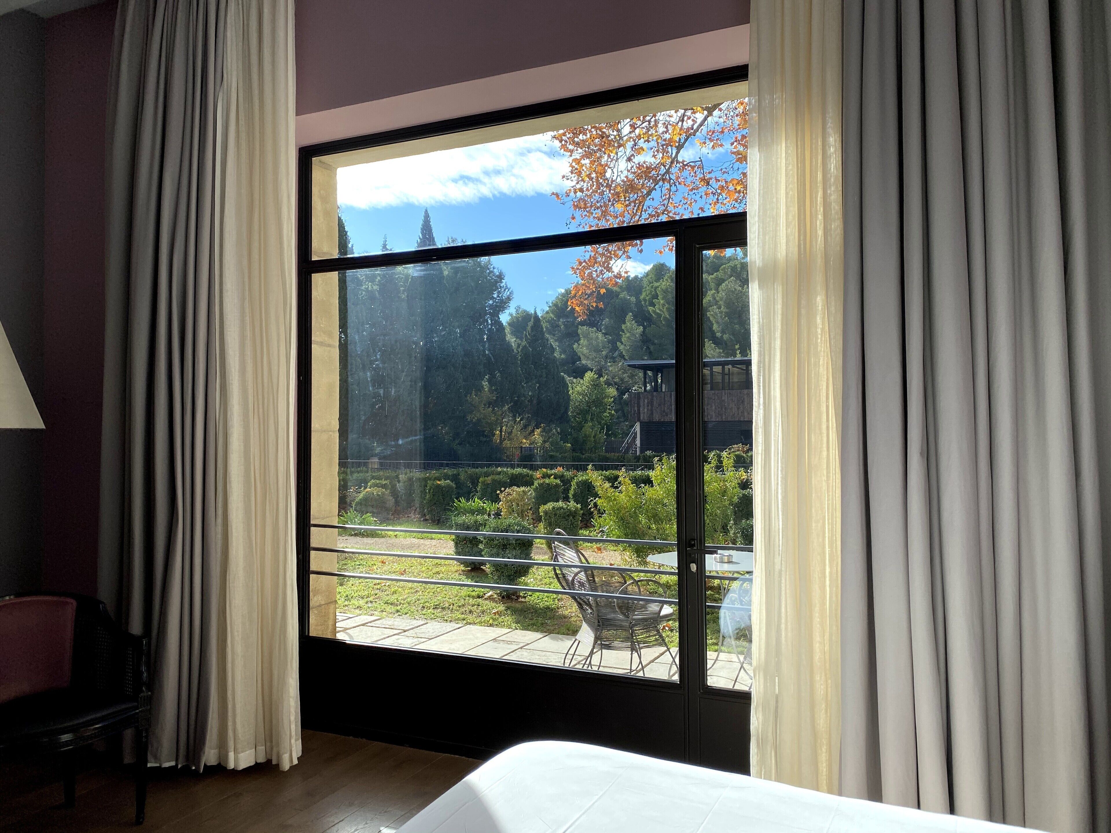 Une pièce dotée d’une grande porte-fenêtre coulissante qui donne sur un espace extérieur avec une terrasse et une vue sur des arbres et un bâtiment.