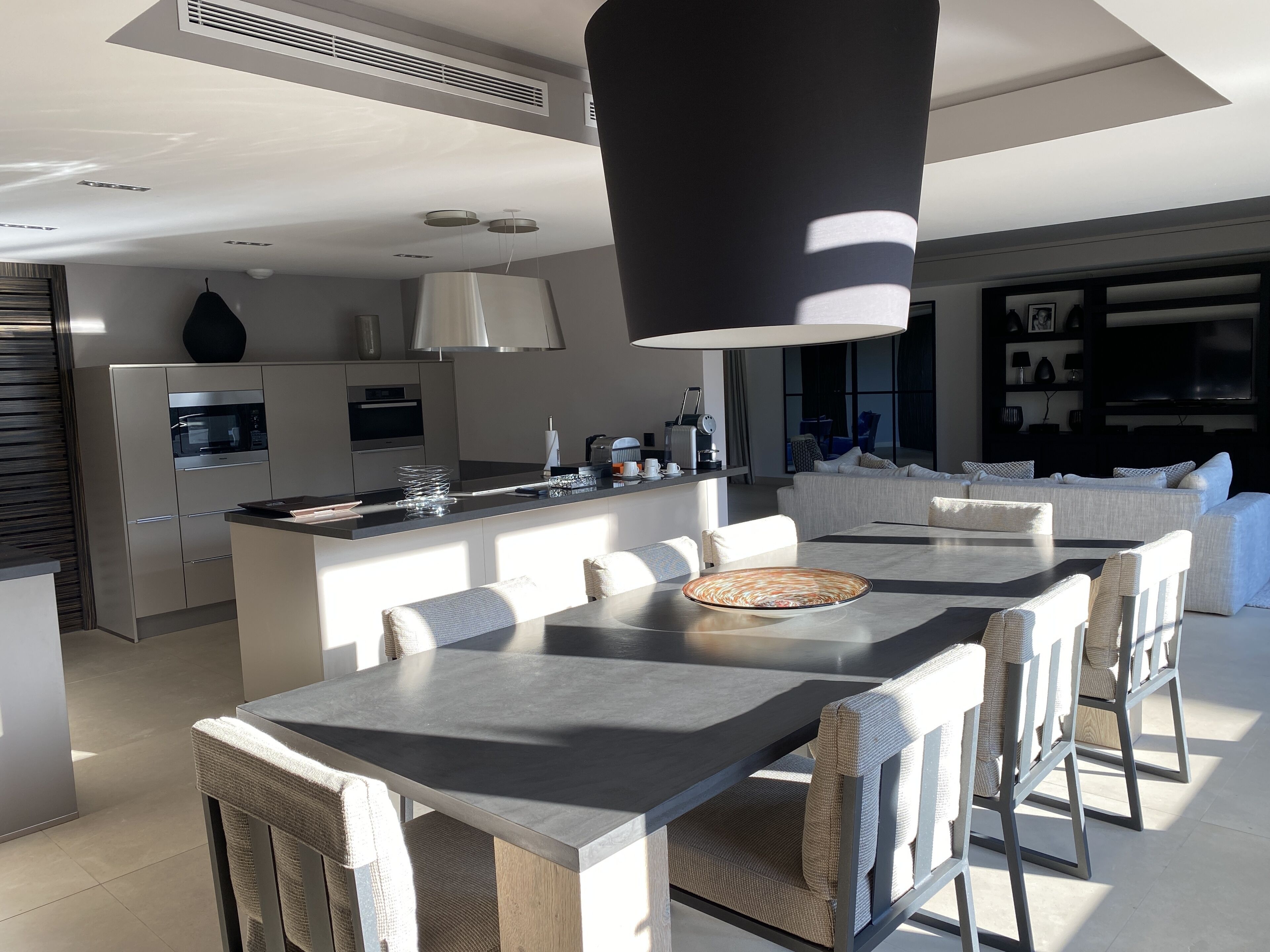 Una cucina moderna con isola centrale, zona pranzo con un tavolo e sedie grandi e un soggiorno con divano e televisione.