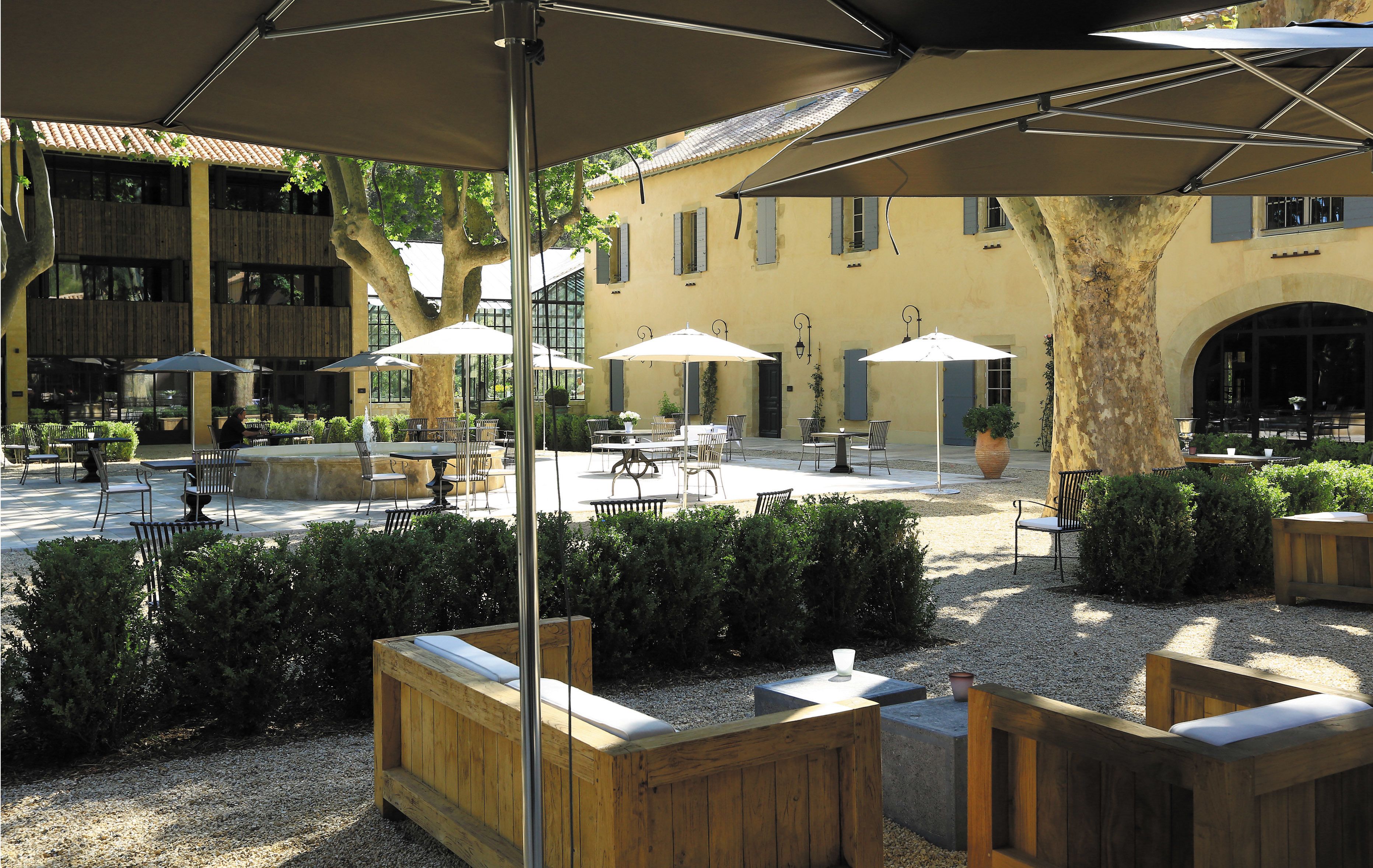 An outdoor seating area with wooden benches and tables, umbrellas, and a building with a tiled roof in the background.