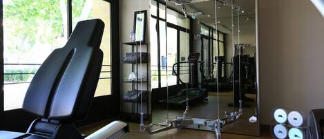 A gym with exercise equipment, a mirror, and a window with a view of trees.
