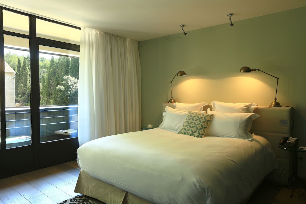 A bedroom with a large bed, two bedside lamps, a bedside table with a phone, and a view through a sliding glass door to a balcony.