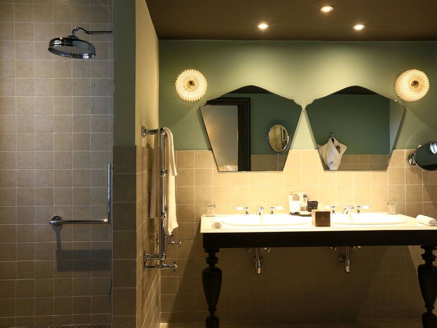 Un baño con ducha, dos lavamanos y un espejo.
