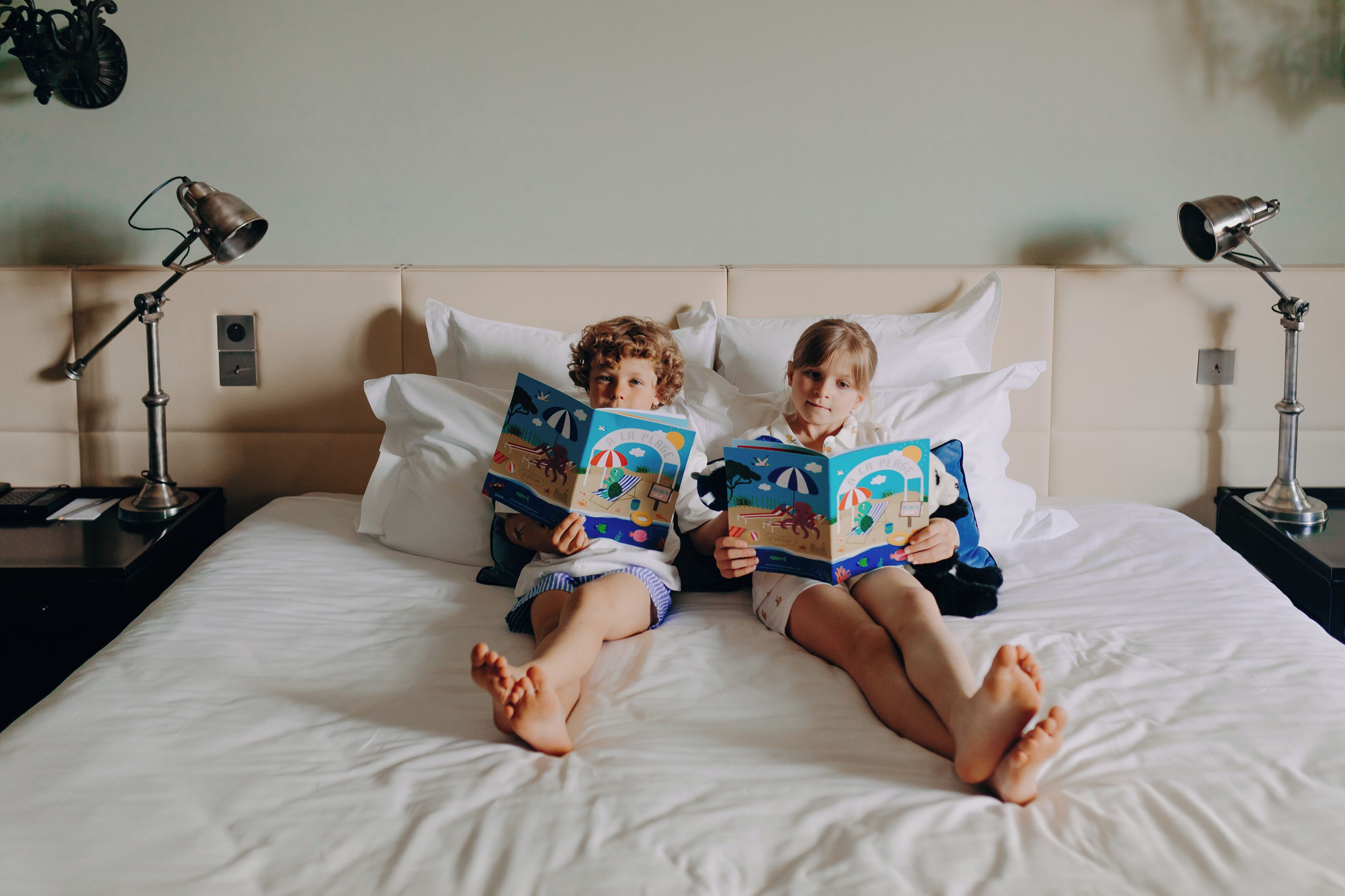 Dos niños acostados en una cama, leyendo libros.