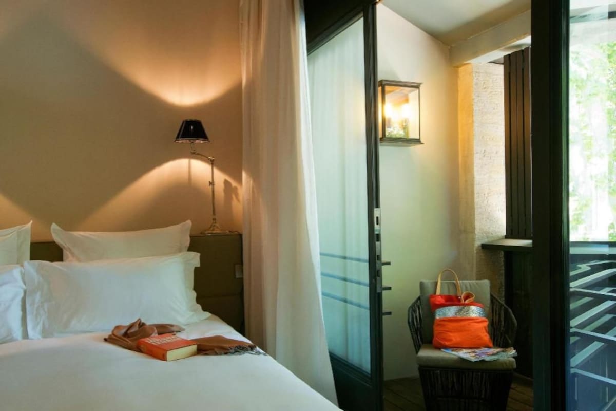 A hotel room with a bed, a nightstand, a lamp, a chair, and a window with a view of the outside.