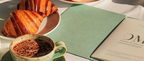A table set with breakfast items including croissants, a grapefruit, a bowl of fruit, a cup of coffee, and a glass of orange juice.