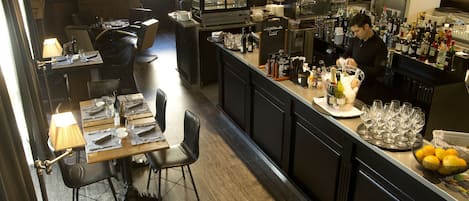 En restaurant med barområde, borde dækket med servietter, bestik og glas, samt en bar med en bartender der laver drinks.