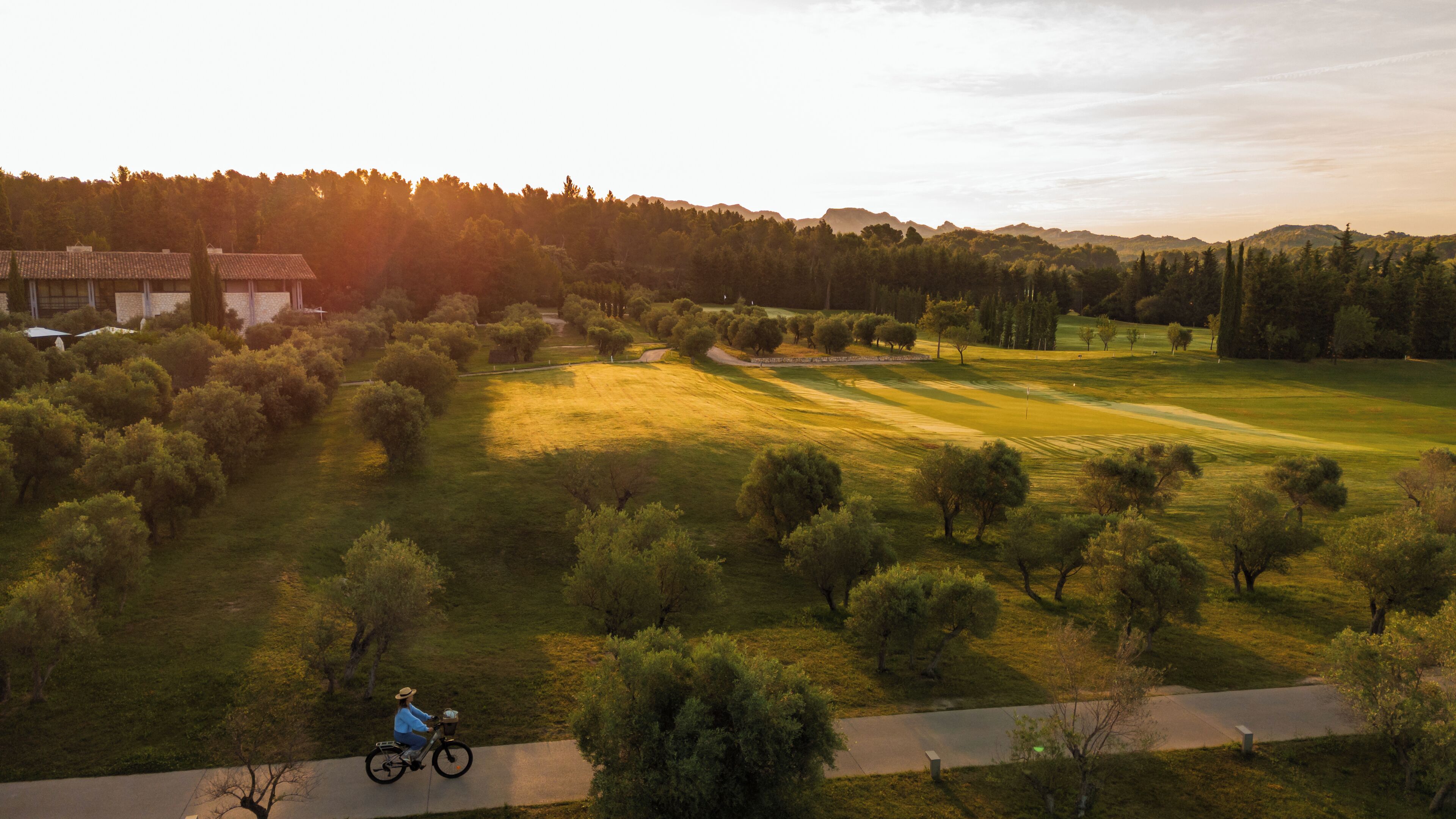 Une personne fait du vélo sur un chemin aménagé qui traverse un parc, avec des arbres et une zone herbeuse.