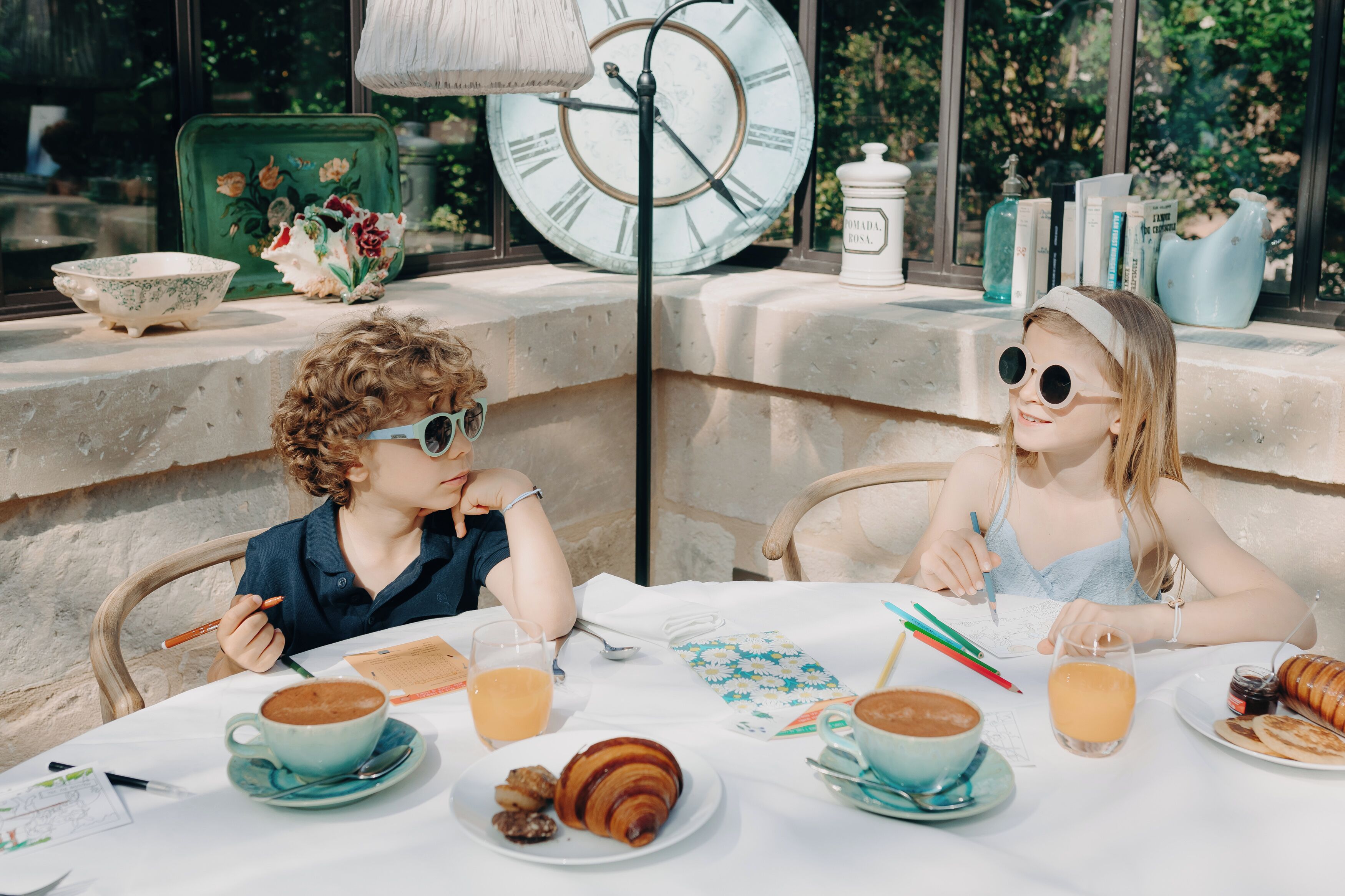 Two children at a table with coffee, pastries, and writing materials.