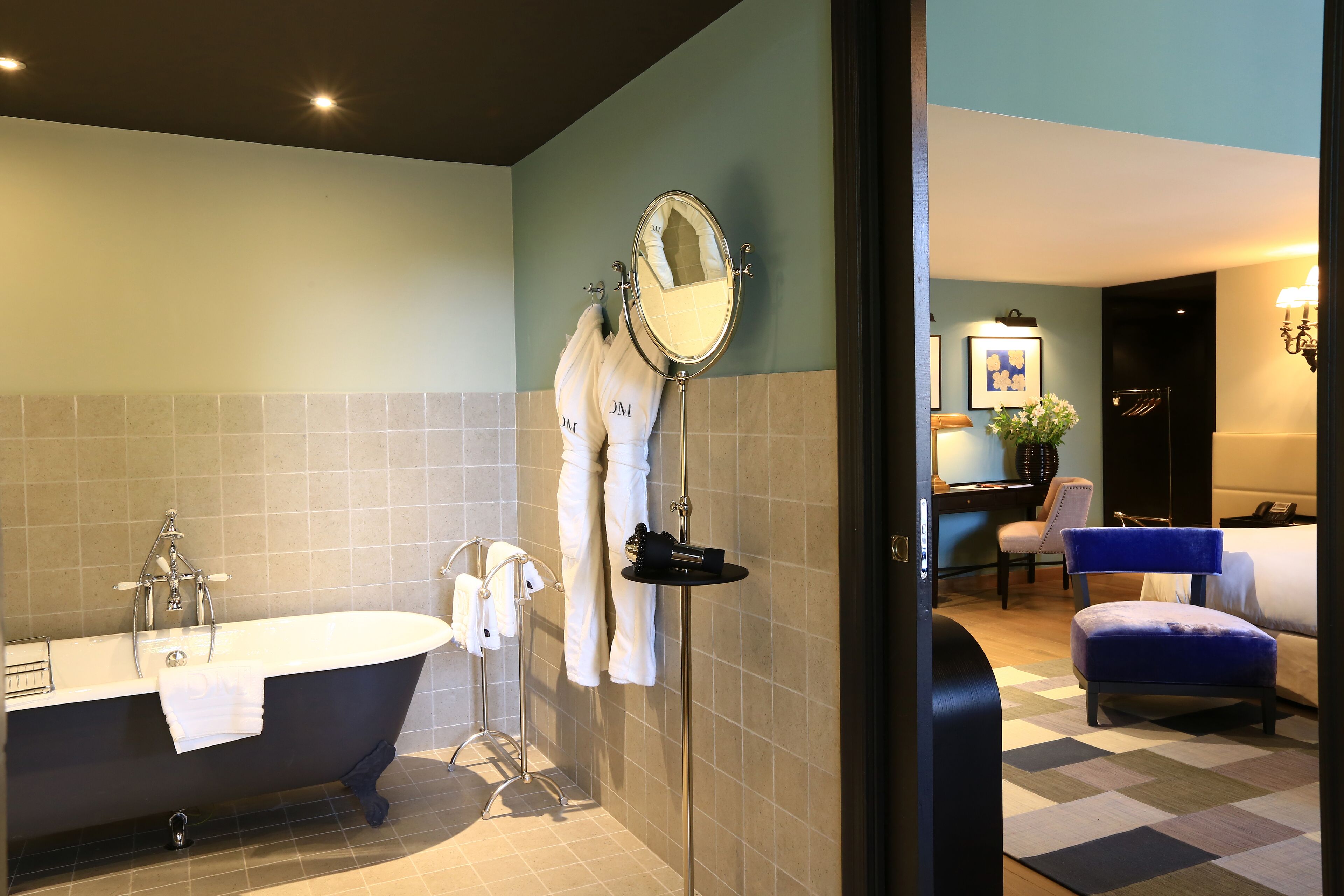 A modern bathroom with a freestanding bathtub, a towel rack with white towels, a mirror, and a small table with toiletries.