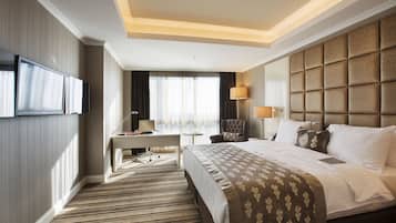 Hotelkamer met een groot bed, een bureau, een stoel, een televisie en een raam met gordijnen.