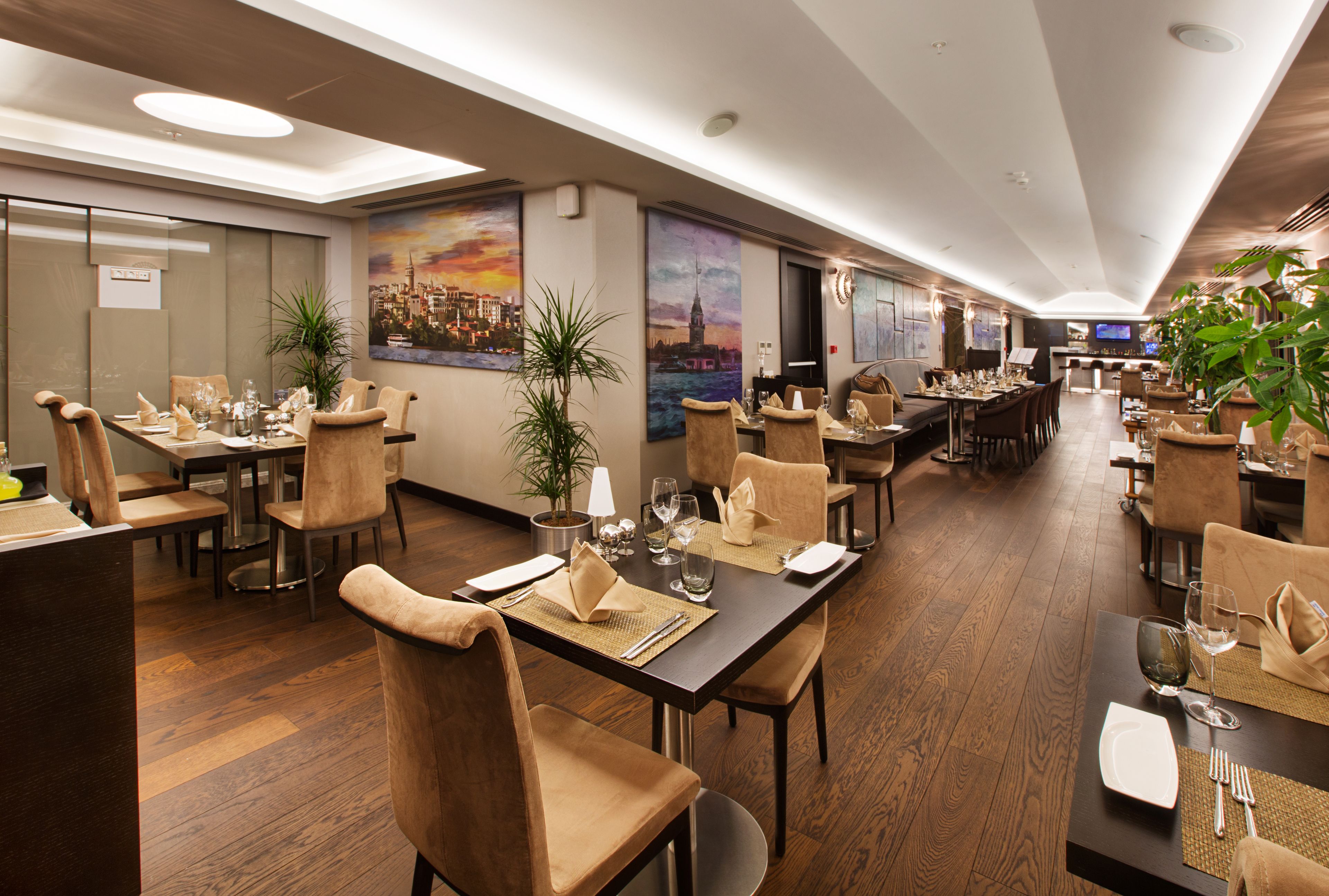 Un comedor amplio de hotel con varias mesas y sillas, ventanas grandes y obras de arte en las paredes.