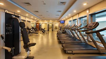 Une salle de sport équipée de tapis de course, d’appareils de musculation et d’un écran de télévision.