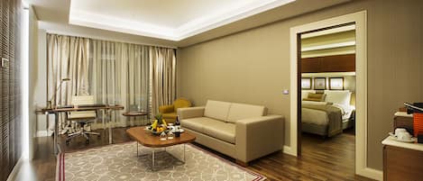 Habitación de hotel con sofá, mesa de comedor, mesa de centro, cama y baño visible a través de una puerta abierta.