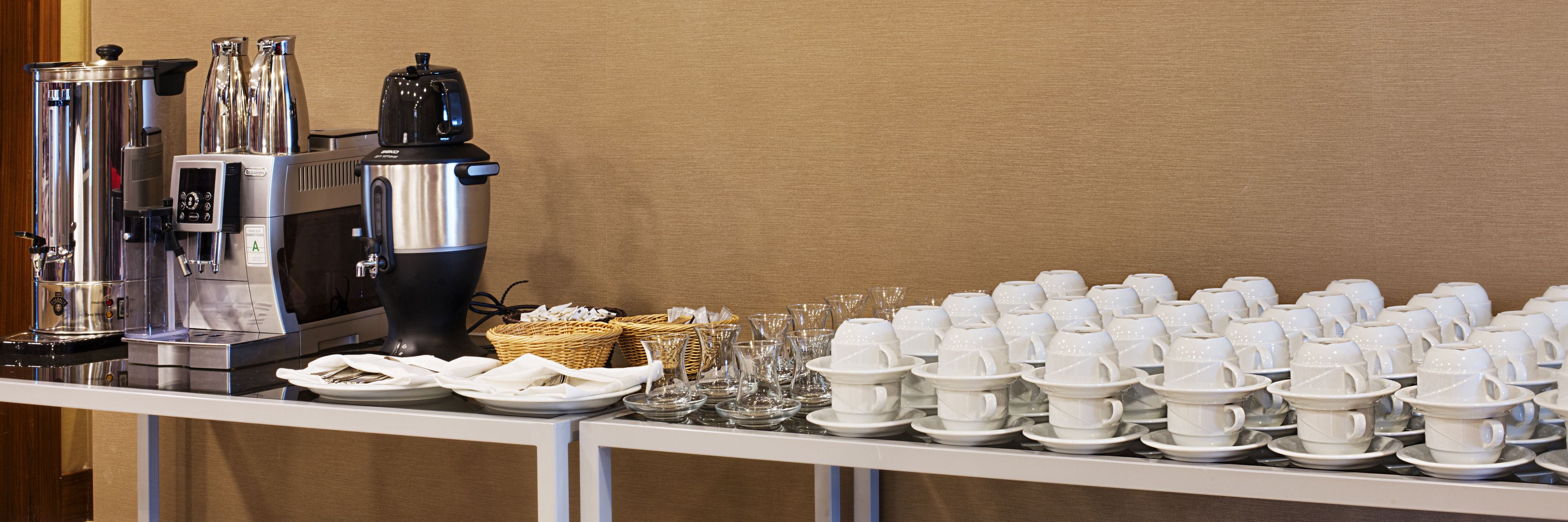 Un buffet avec des machines à café, des tasses blanches et de la verrerie.