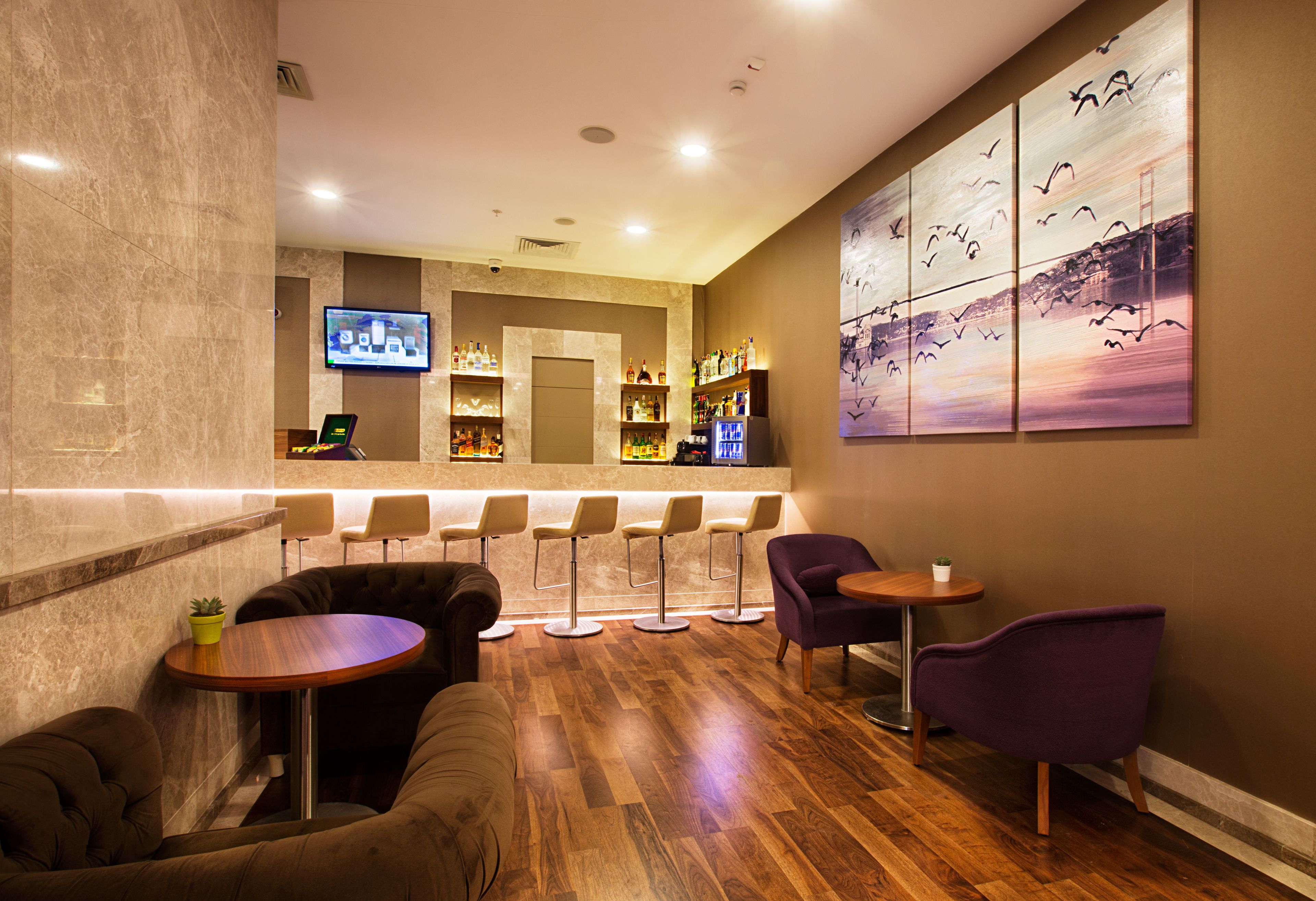 A bar area with wooden flooring, bar stools, and a television screen.