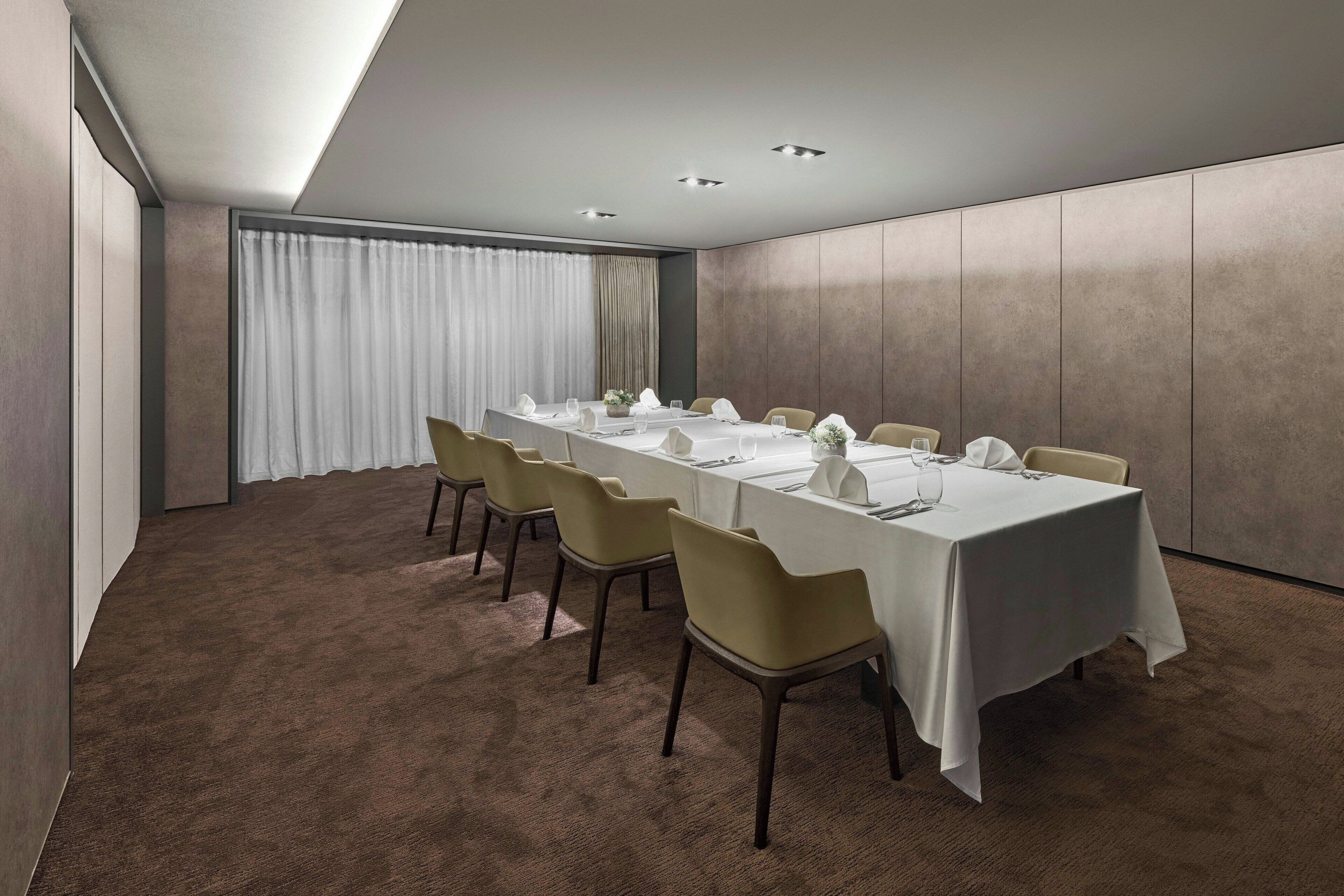 A conference room with a long table set for a meeting, beige chairs, and a carpeted floor.