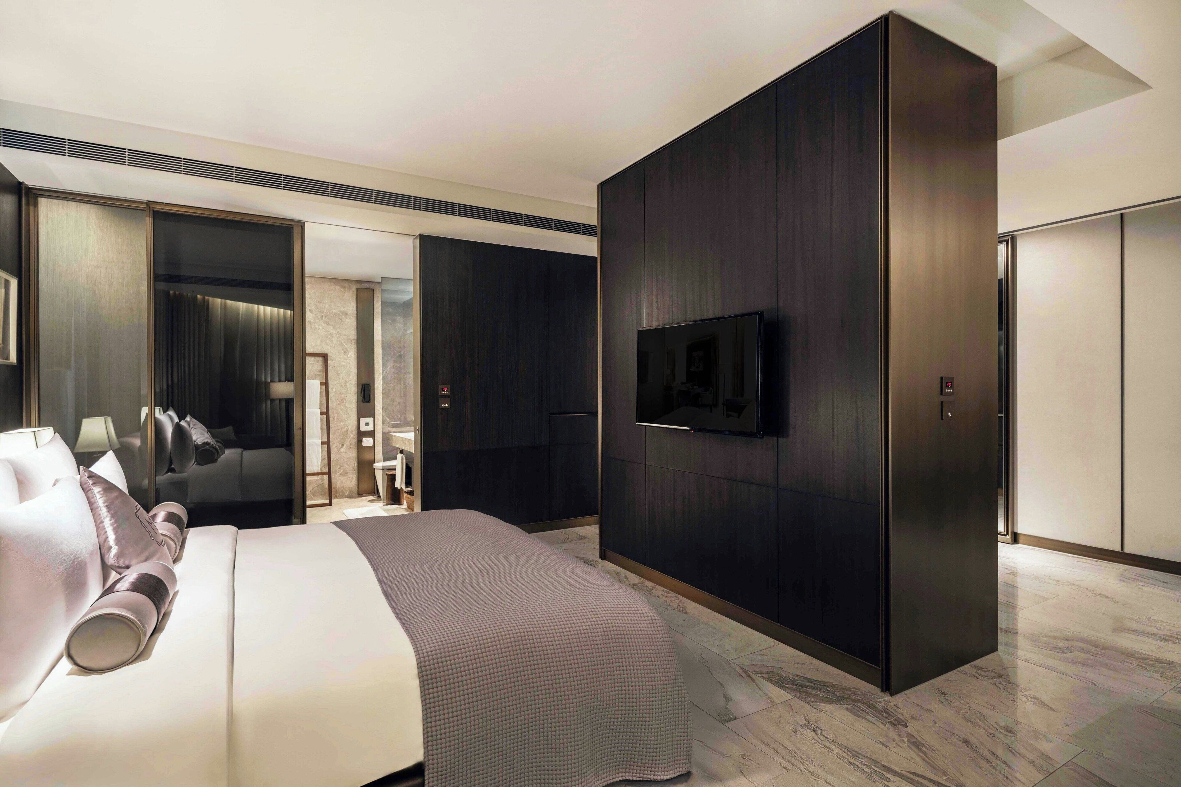 A modern hotel room with a large bed, a flat-screen TV mounted on the wall, and a wardrobe with a mirror.