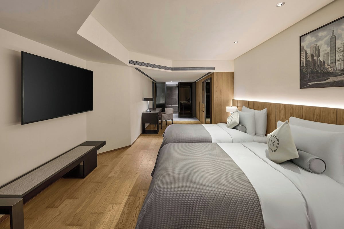 A modern hotel room with a large bed, a flat-screen TV, a bench, and a cityscape painting on the wall.
