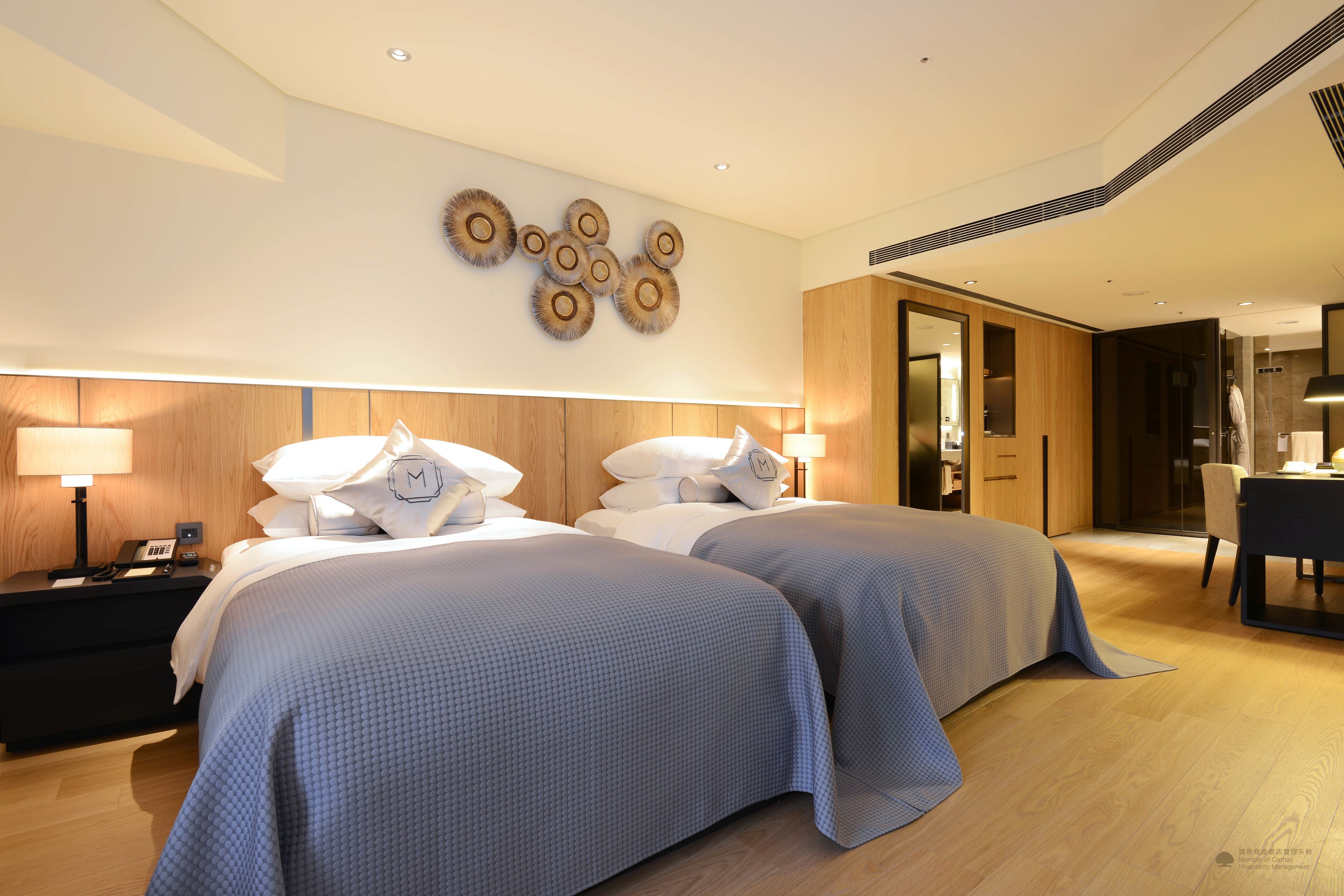 Une chambre d’hôtel moderne avec deux lits, une tête de lit en bois, une œuvre d’art accrochée au mur et un bureau avec une chaise.