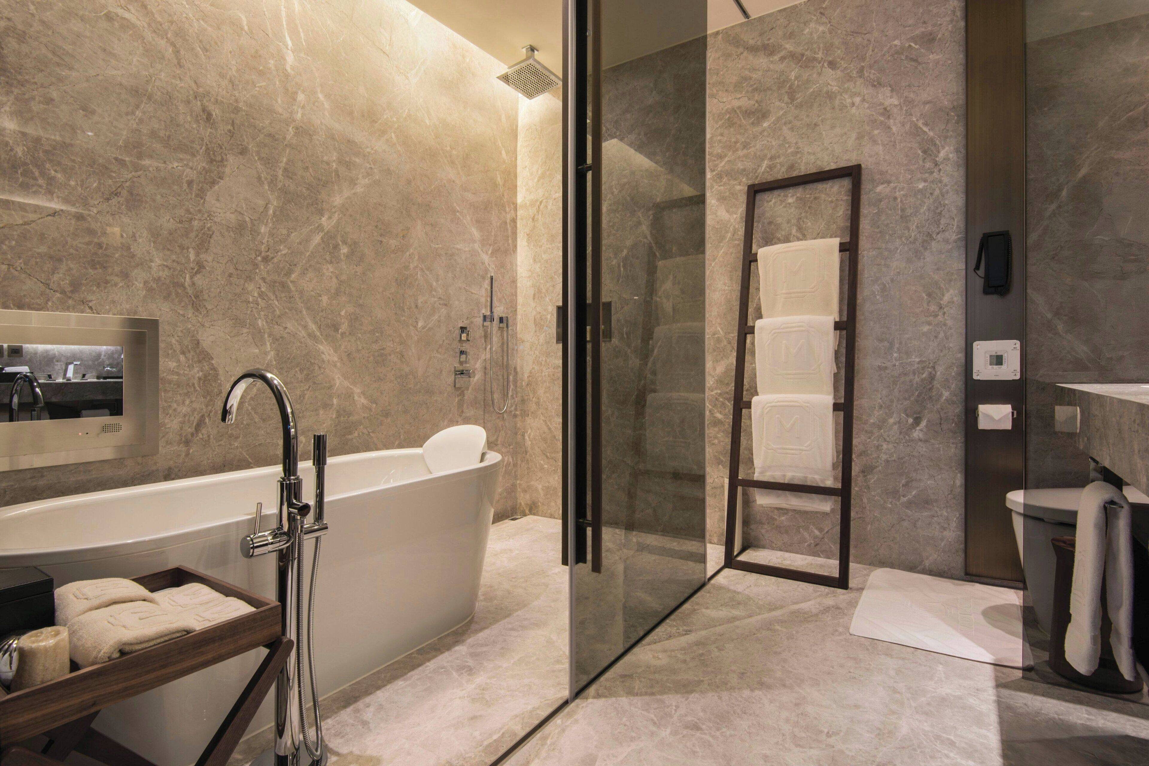 A modern bathroom with a freestanding bathtub, a glass-enclosed shower, and a marble-tiled wall.