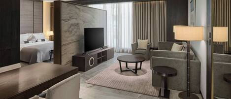 A modern hotel room with a bed, a TV, a sofa, a coffee table, and a dining area.