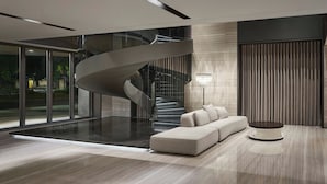 A modern living room with a curved staircase, a sectional sofa, and a round coffee table. - Madison Taipei, a Tribute Portfolio Hotel (Taipei)