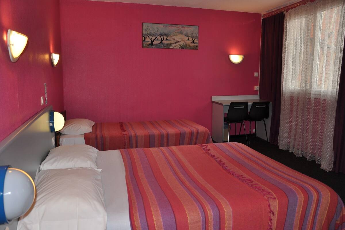 A hotel room with two beds, a desk, and a chair.