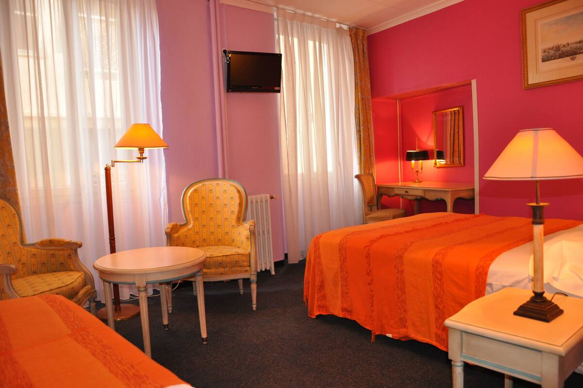 A hotel room with a bed, a chair, a table, a lamp, a television, and a mirror.