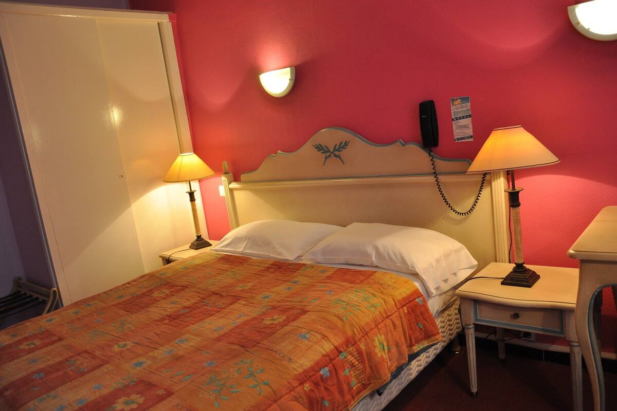 A bed with a floral bedspread, two bedside lamps, a nightstand, and a wall-mounted telephone.