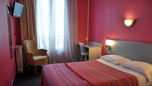 Ein Hotelzimmer mit Bett, Schreibtisch, Stuhl, Fernseher und einem fenster mit Vorhängen.