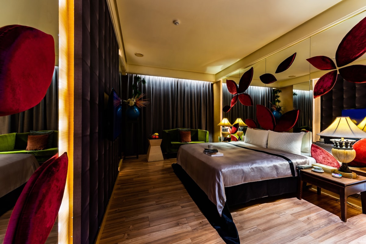 Une chambre d’hôtel moderne dotée d’un grand lit, d’un coin salon avec un canapé et des fauteuils, et d’une table à manger avec une lampe.