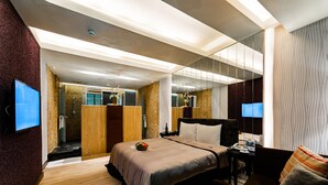 Una habitación de hotel moderna con una cama grande, un escritorio, una silla, un televisor y un baño con ducha e inodoro.
