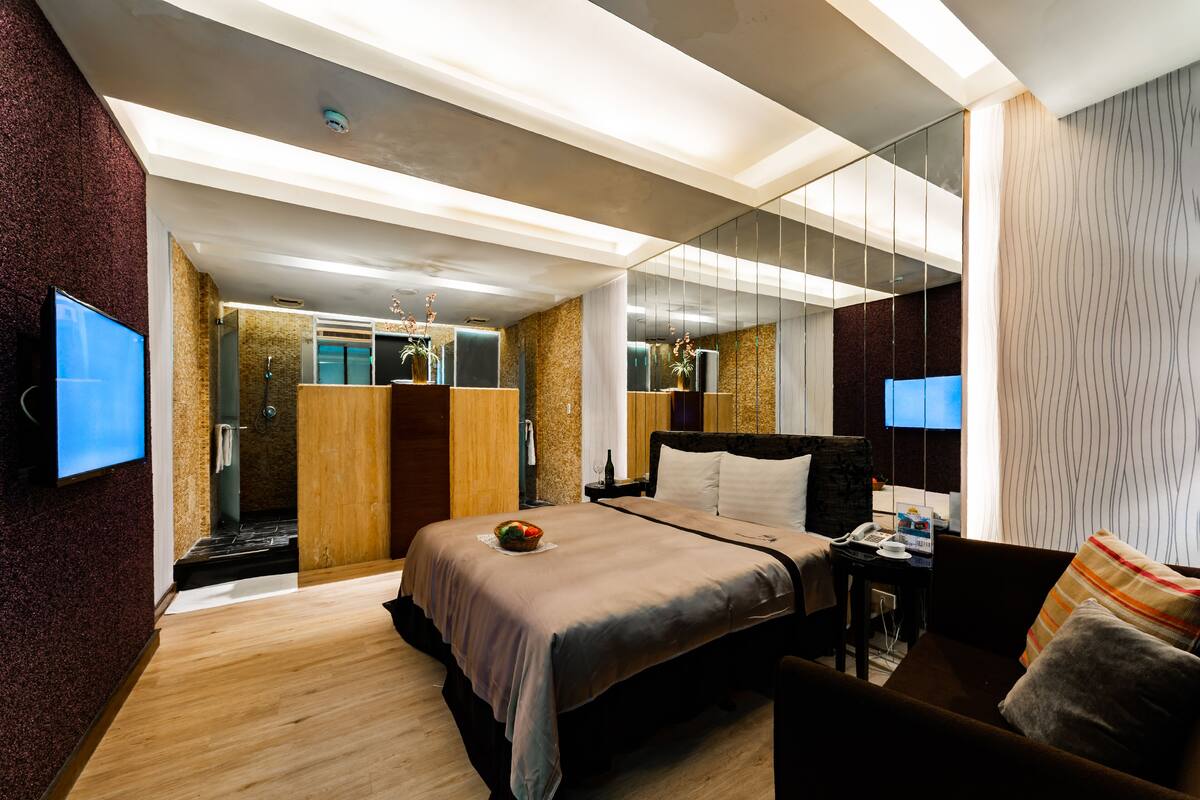 Una habitación de hotel moderna con una cama grande, un escritorio, una silla, un televisor y un baño con ducha e inodoro.