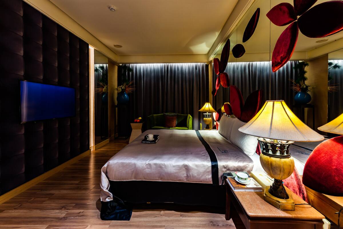 Una habitación de hotel moderna con una cama grande, un televisor de pantalla plana y una decoración floral roja original.
