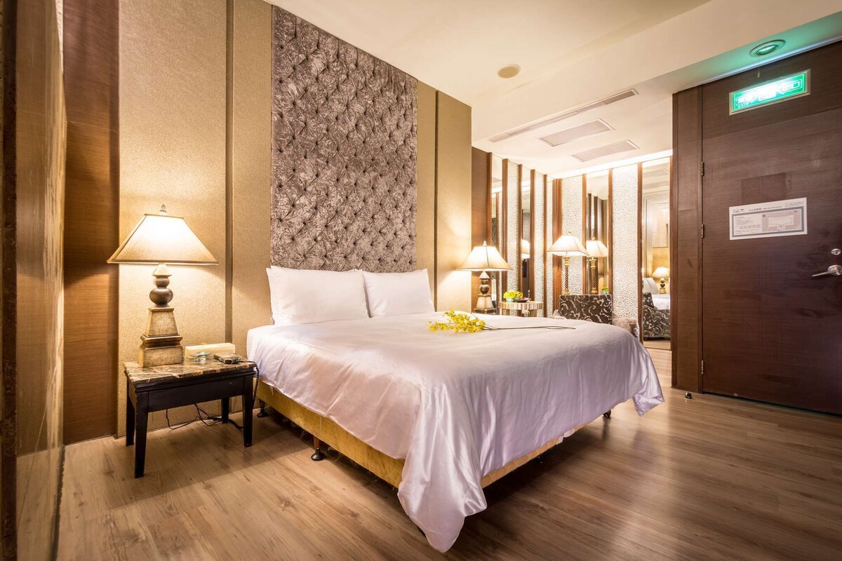 Une chambre d’hôtel avec un grand lit, une table de chevet, une lampe et une porte portant un panneau indiquant la sortie de secours.