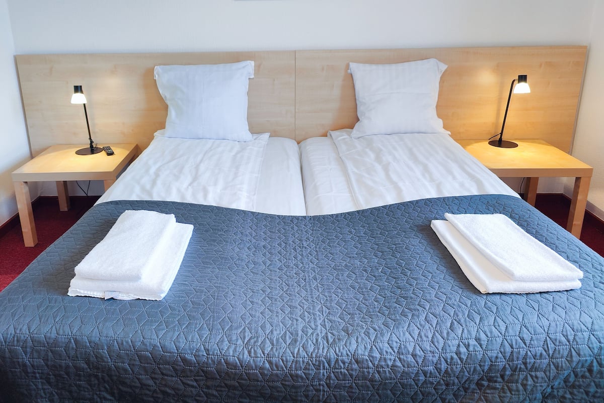 A double bed with a blue quilt, two white pillows, and two bedside tables with lamps.