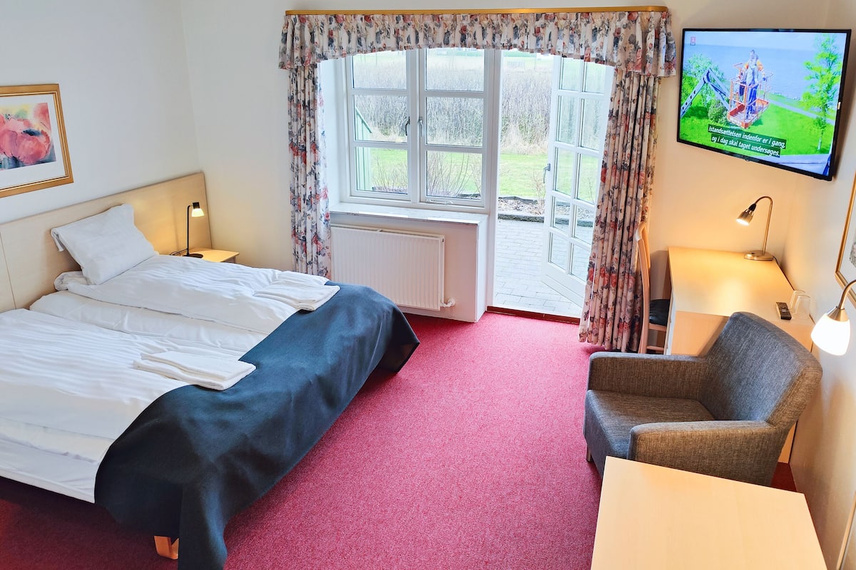 A hotel room with a bed, a desk, a chair, a television, and a window with curtains.