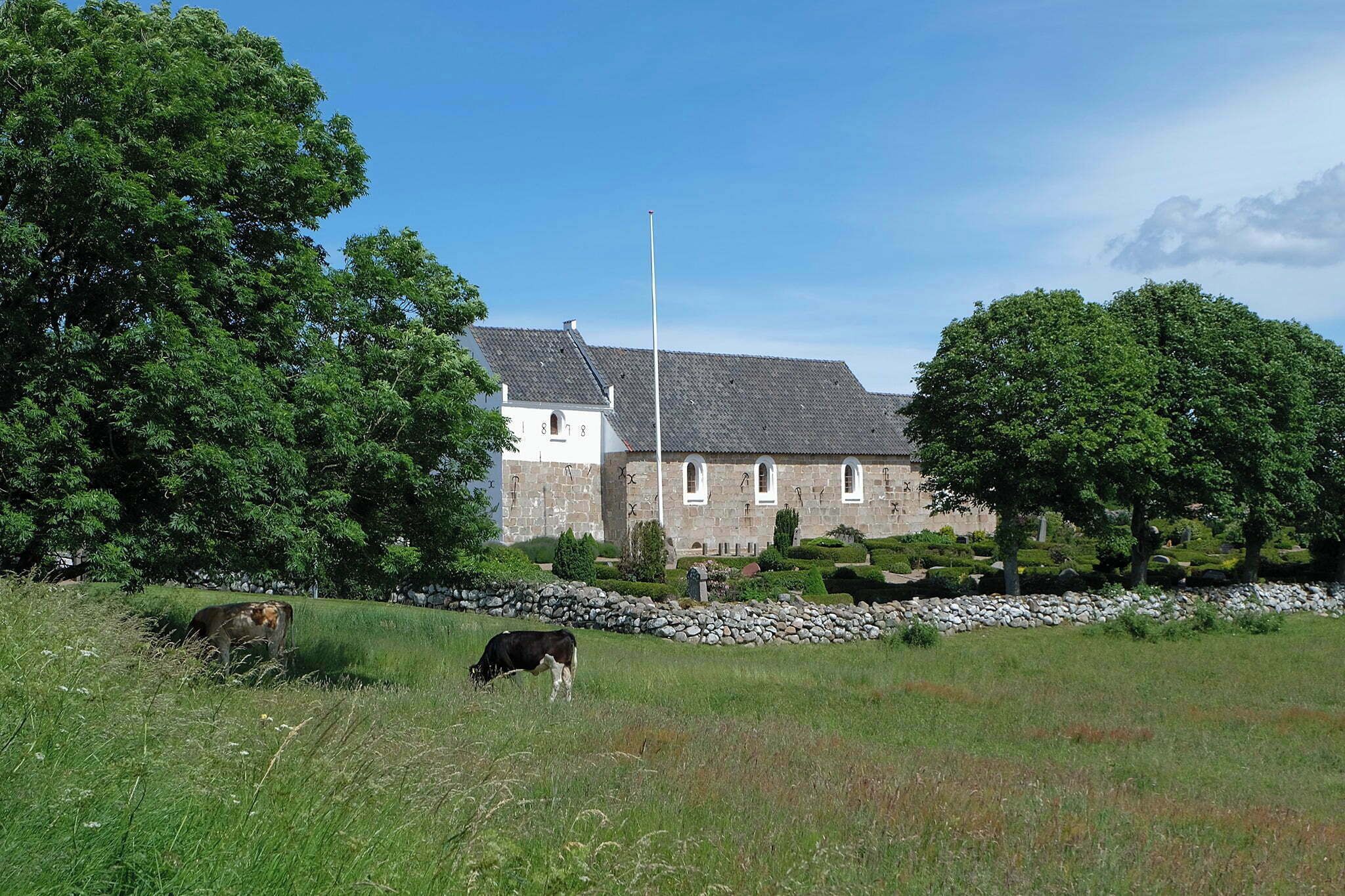 A stone building with a flagpole, surrounded by trees and a stone wall.