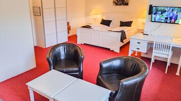 A hotel room with a bed, two black leather chairs, a white table, a desk, and a television on the wall.
