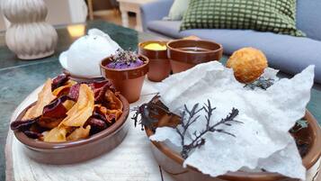 Et bord med forskellige retter, heriblandt en skål chips, en skål der ligner dessert, og to små terracotta-potter med et lilla stof og et gult stof.