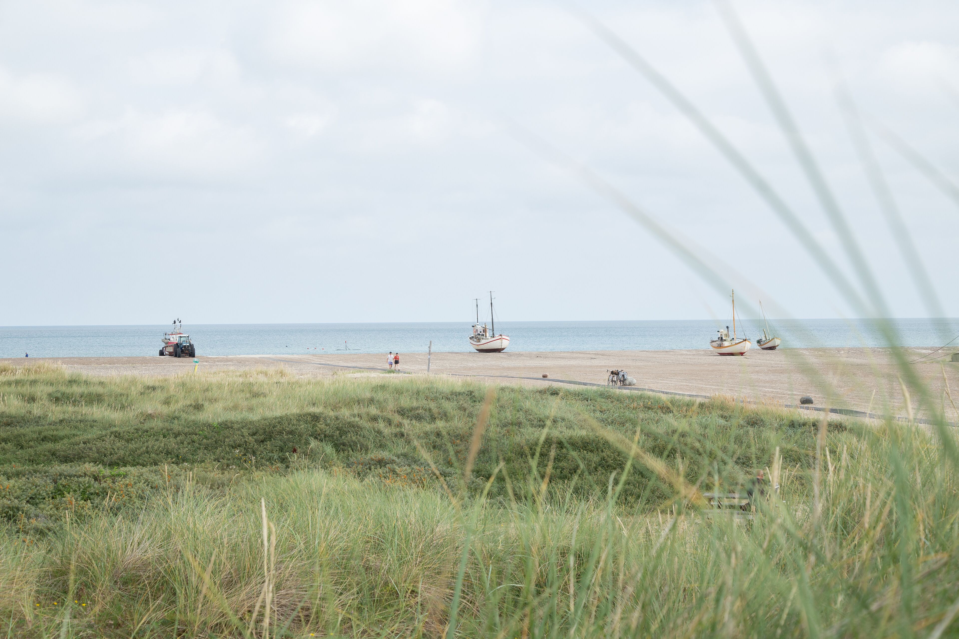 Una playa con barcos y un vehículo en la arena.