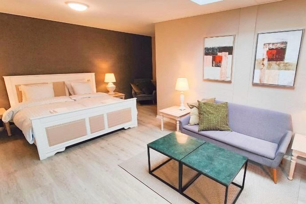 A hotel room with a bed, a sofa, a coffee table, and two bedside tables with lamps.