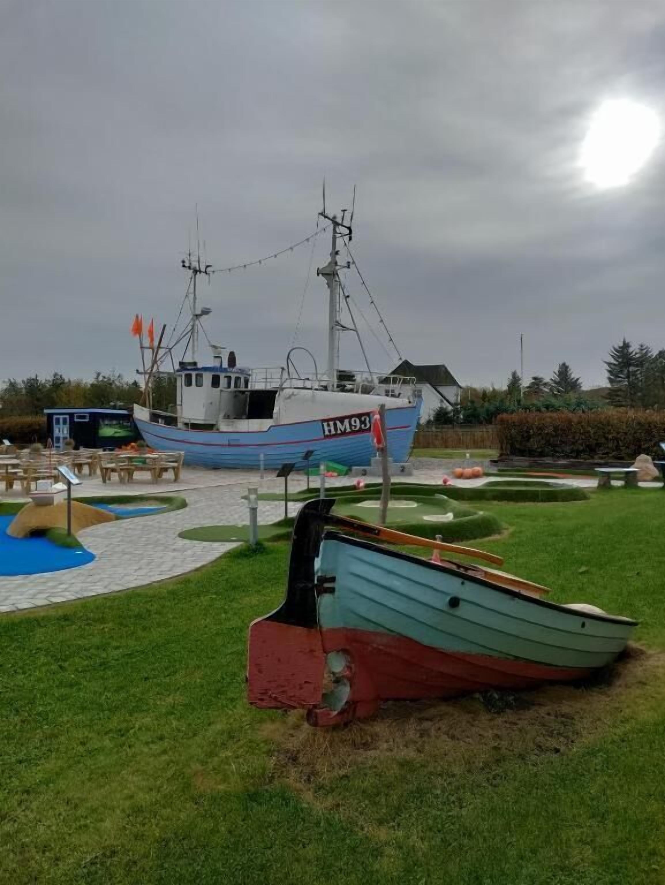 A boat with the registration number HM93 docked in a grassy area with a small pond and picnic tables.