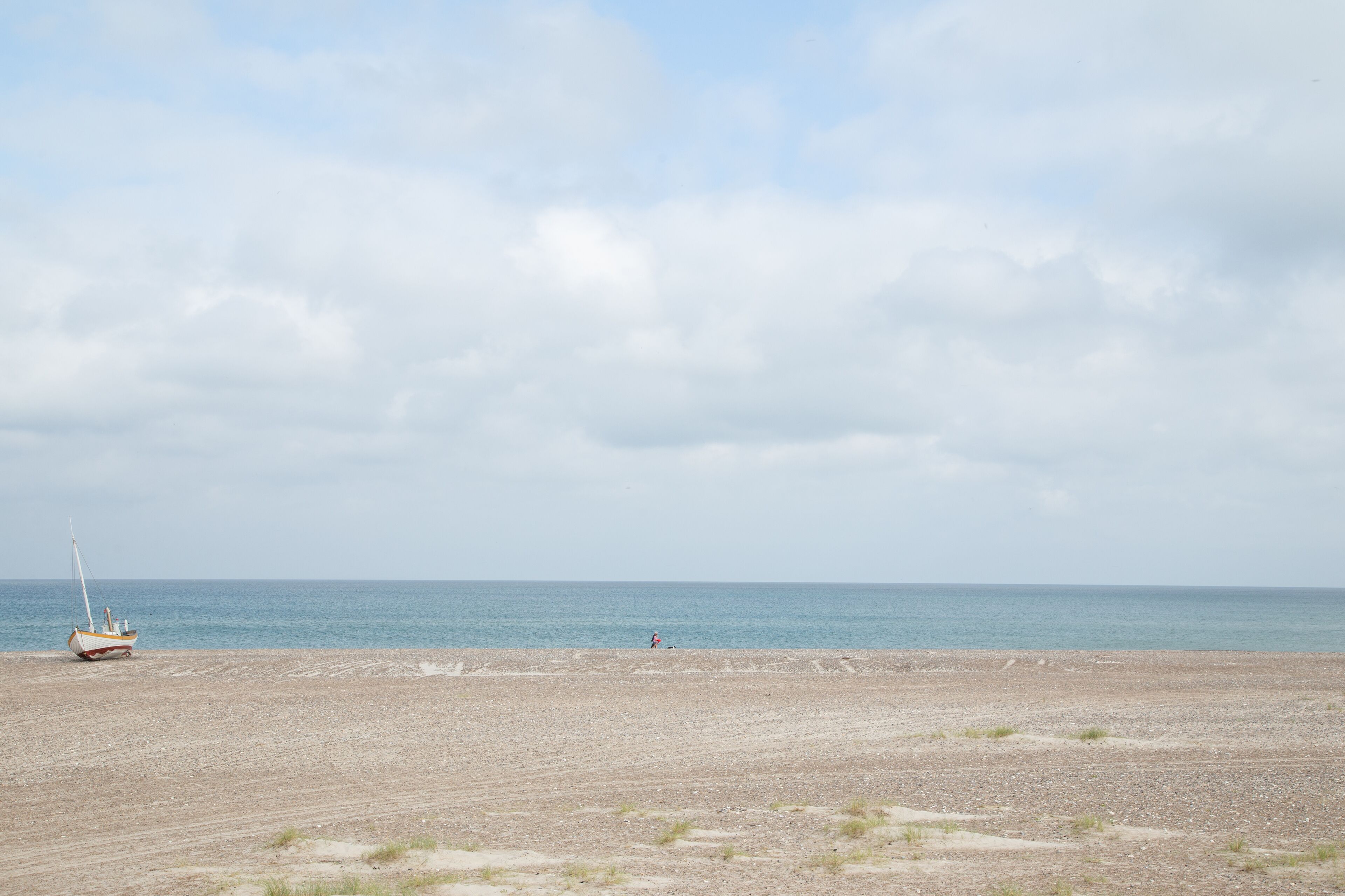 A beach with a small boat and a person in the distance.