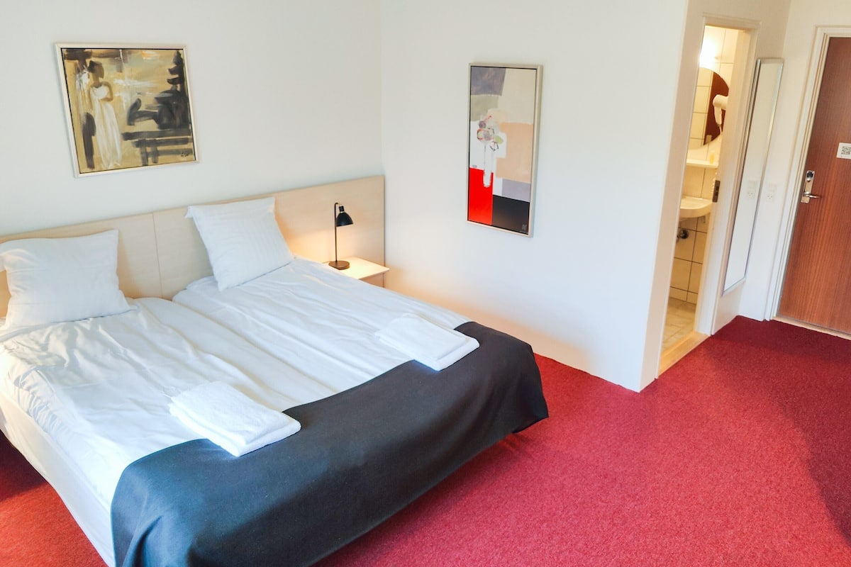 A hotel room with a bed, a nightstand, a lamp, and two paintings on the wall.