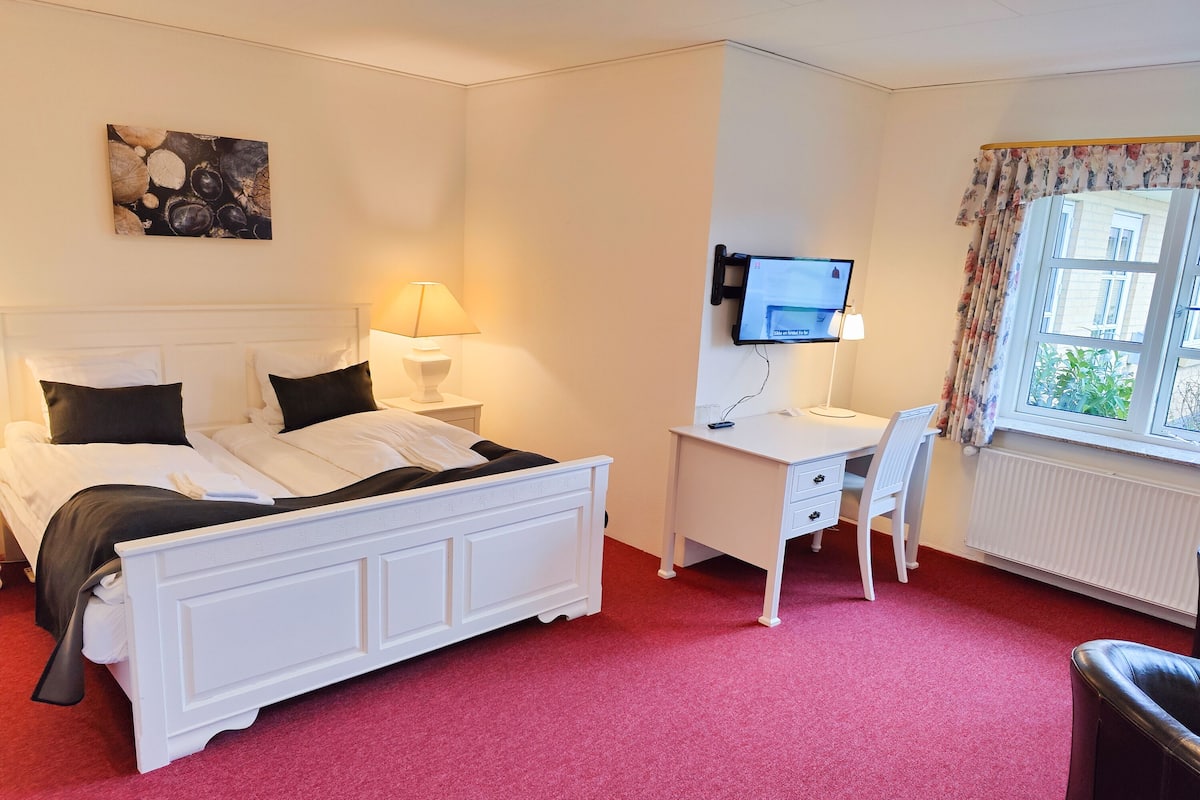 A hotel room with a bed, a desk, a chair, a TV, and a window with curtains.